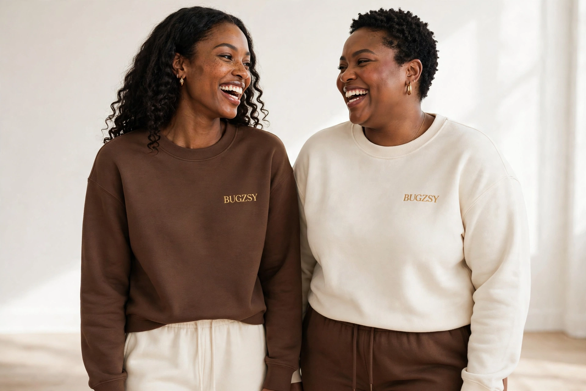 Two Black models laughing together in chocolate and cream Bugzsy crewnecks